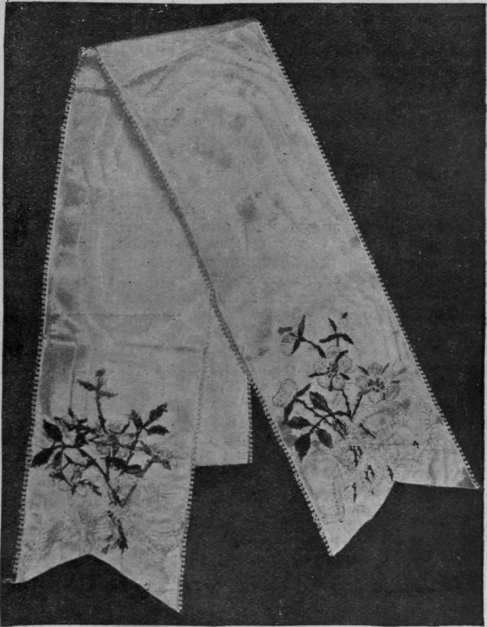 An embroidered ribbon for table decoration. Wild rose sprays are worked upon white moire silk ribbon, and the design is completed by a true lover's knot in pale blue