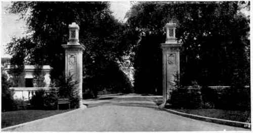 An elaborate entranceway of concrete. The columns carry artistic receptacles for electric lights.